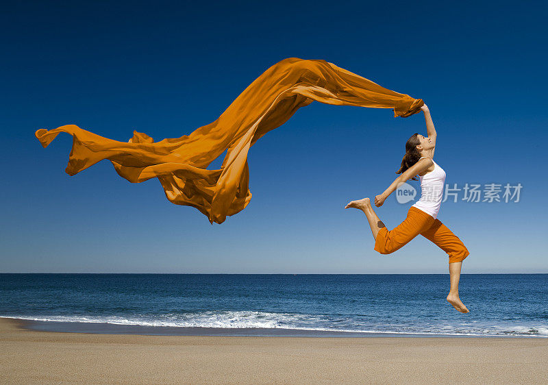 戴着橙色围巾的女人在海滩上蹦蹦跳跳