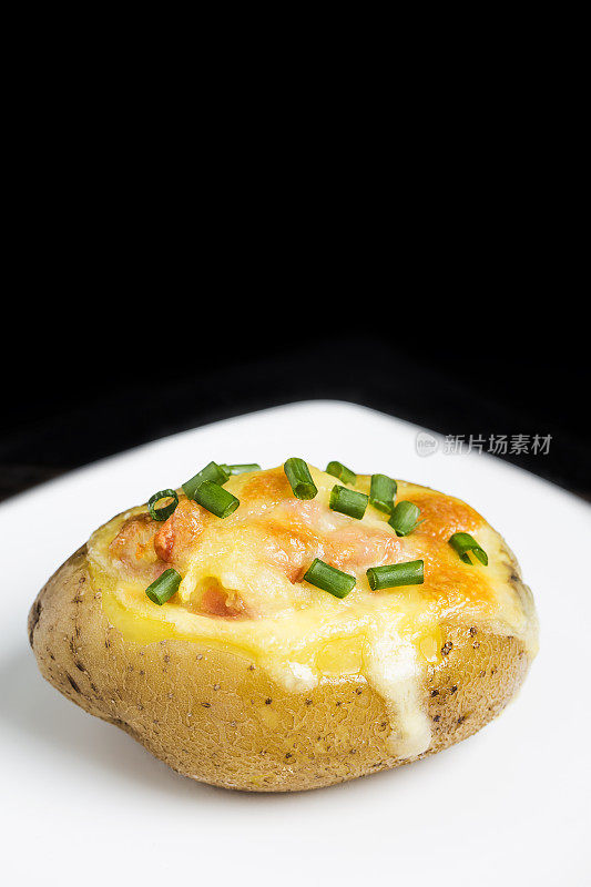 一个热烤土豆的特写，上面有酸奶油，培根，葱和切达干酪。