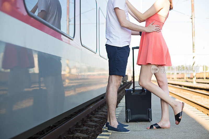 一对年轻的白人夫妇站在火车站，站在火车旁边