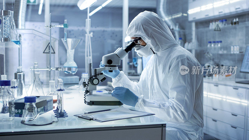 在一个安全的高水平研究实验室里，穿着工作服的科学家在显微镜下检查培养皿。
