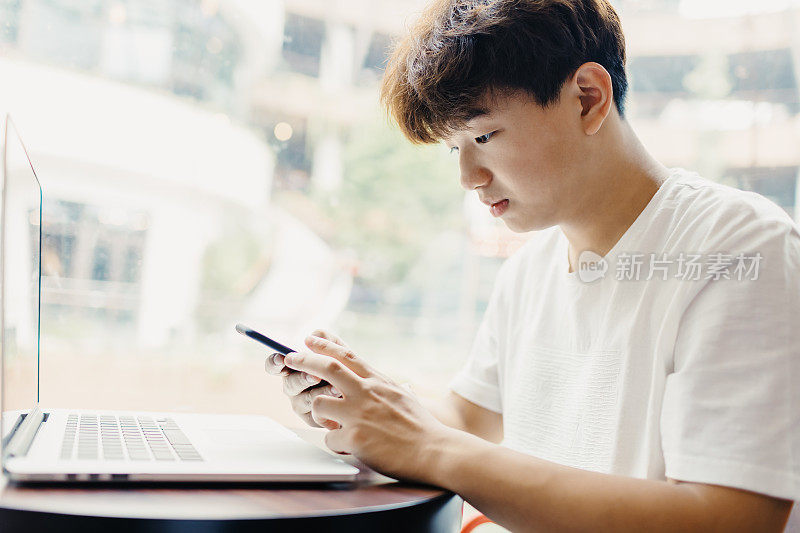 一名亚洲少年在咖啡馆里玩智能手机，上海。