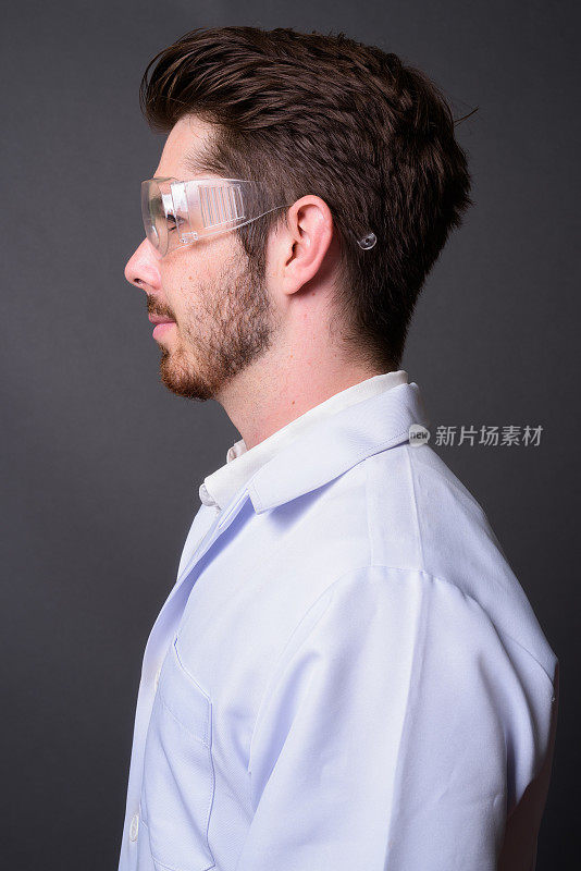 年轻的胡子英俊的男子医生戴着保护眼镜对抗灰色的背景