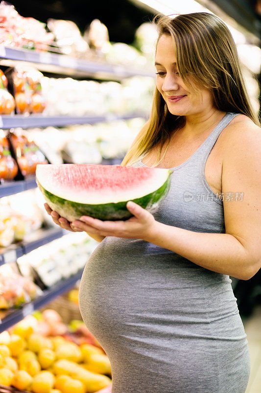 微笑的孕妇在超市挑选西瓜