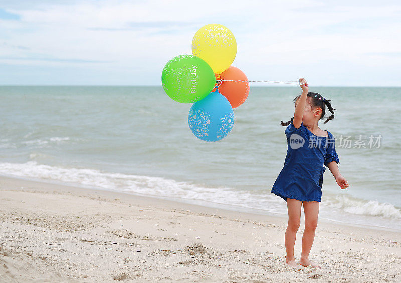 孩子们在海滩上拿着彩色气球。