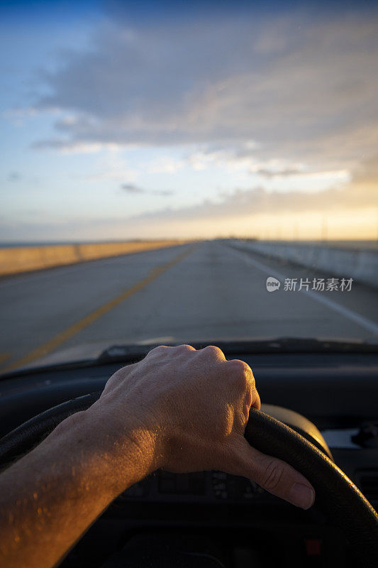 日出时分，高速公路上，驾驶员的手放在方向盘上