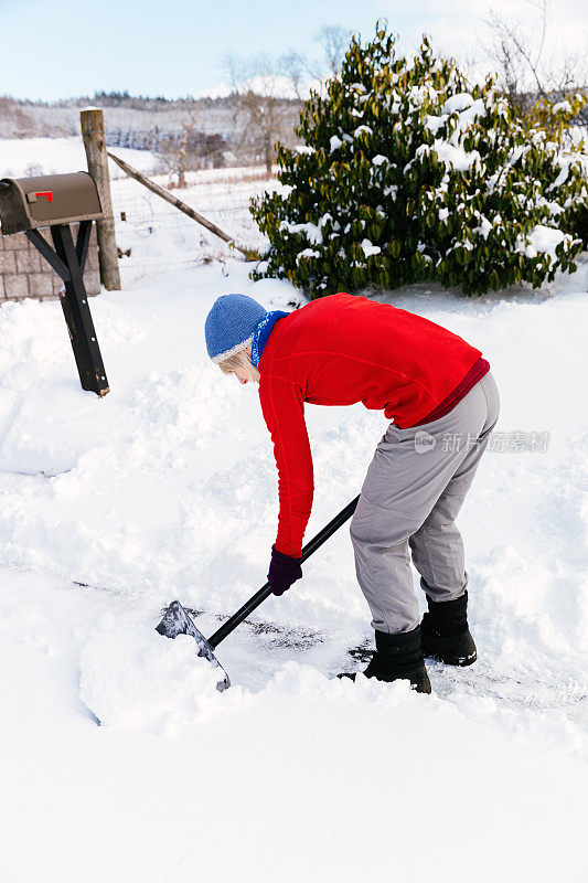 老妇人正在用雪铲清理积雪