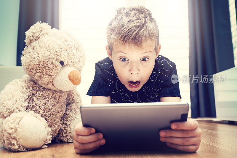 一个男孩和一只泰迪熊正在用平板电脑看电影