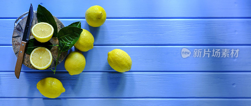 一组柠檬用锋利的刀放在砧板上，砧板上的一个柠檬被切成横截面，设置在一个抽象的古老的风化的充满活力的蓝色和绿色木制背景上。