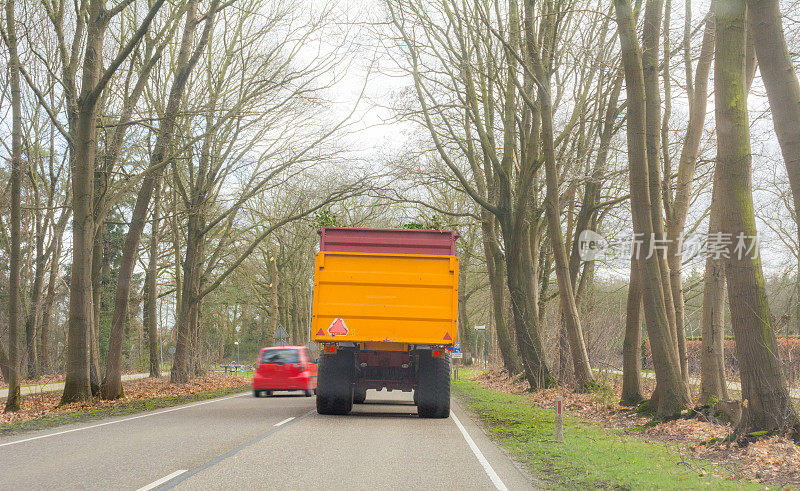 一辆红色轿车在乡村公路上超越带拖车的拖拉机