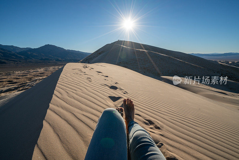 女性日落时在沙丘上放松的个人视角;脚视图;人们旅游度假放松的概念