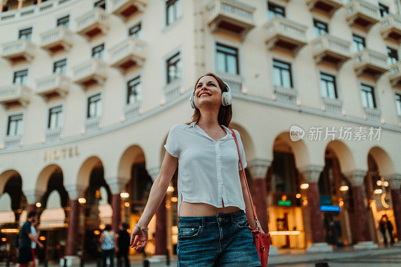 快乐的女人戴着耳机在城市的街道上听音乐