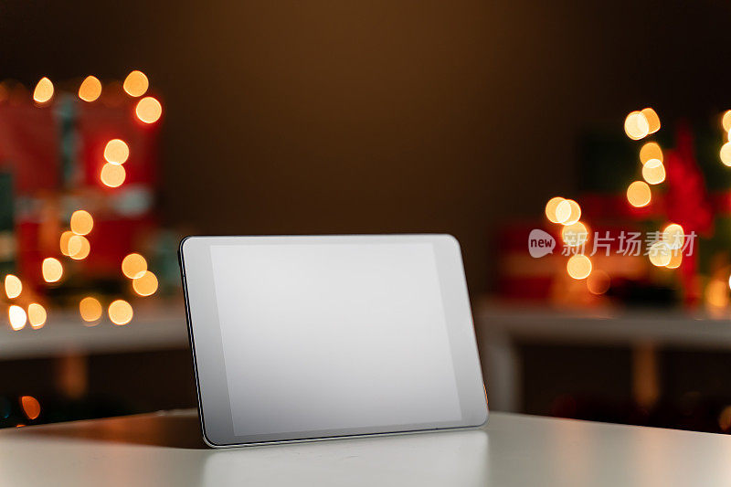 白色桌子上的数码平板，背景里的散焦圣诞灯，散焦