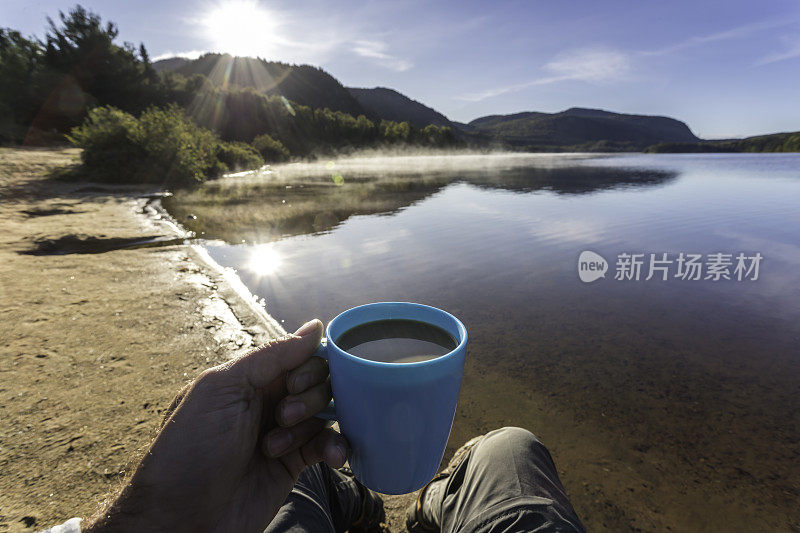 在秋天露营的湖边喝咖啡的男人