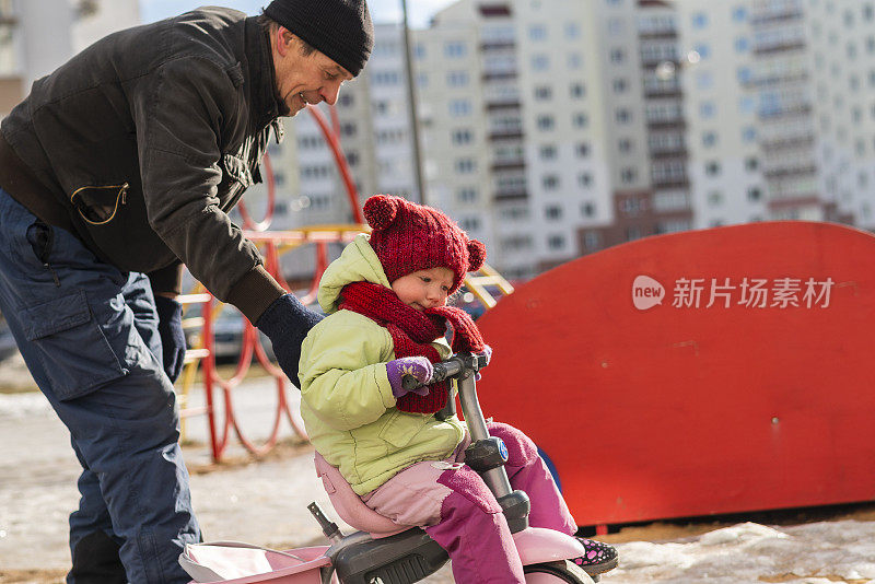 70岁的老人，活跃的爷爷，教他的孙女，2岁的小女孩，如何骑自行车在寒冷和阳光明媚的冬日散步。