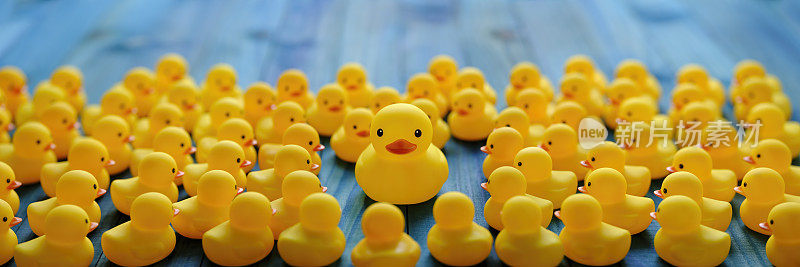 大黄鸭以木板桌为背景，一大群黄色小橡皮鸭围绕着大黄鸭，概念形象从人群中脱颖而出。