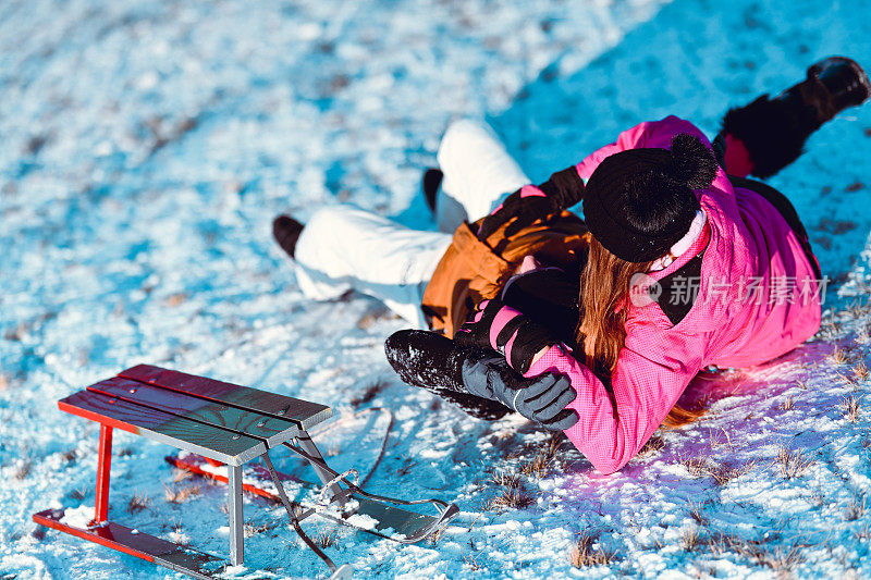 男孩和女孩滑下坡后从雪橇上摔下来