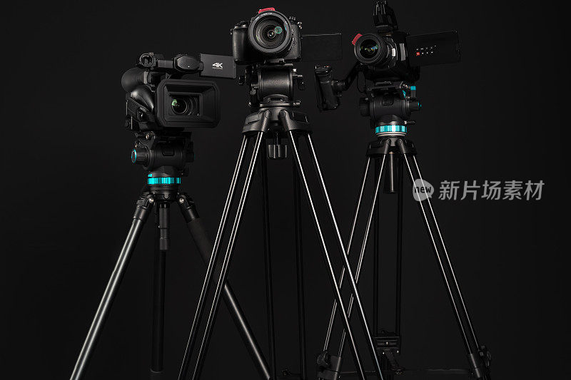 三种不同类型的视频影院摄影相机在三脚架上，黑色背景，低角度视角