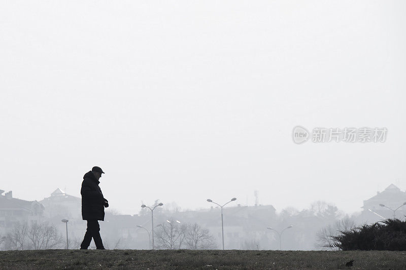 在一个雾蒙蒙的冬日里，一个老人独自行走的剪影