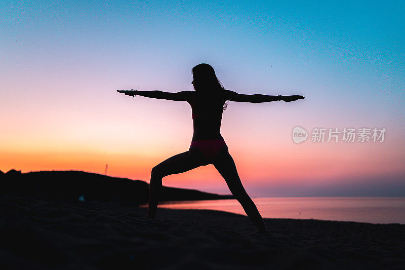 黄金时间日落时分，在海滩上做瑜伽的女人的剪影。