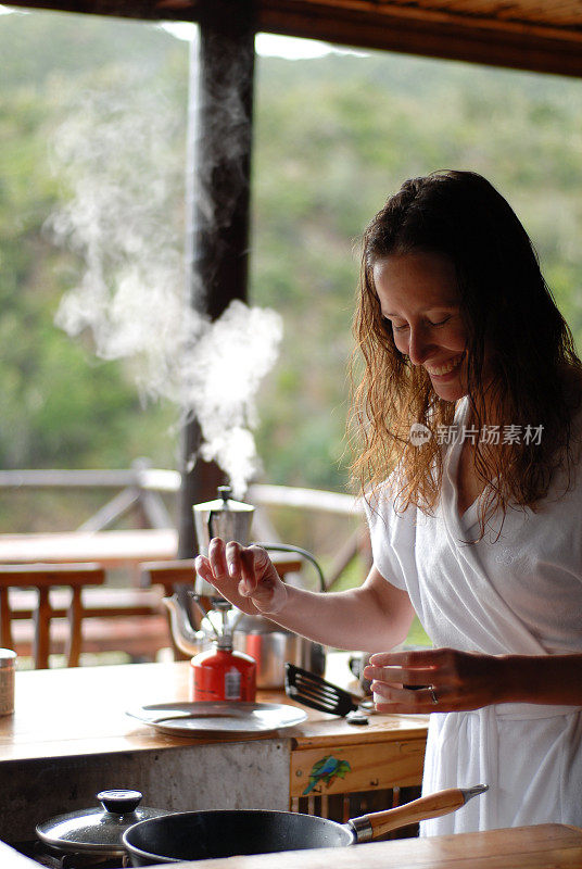 在一个露天门廊的小木屋里，一个美丽的女人正在做饭，咖啡壶在她身后冒着热气
