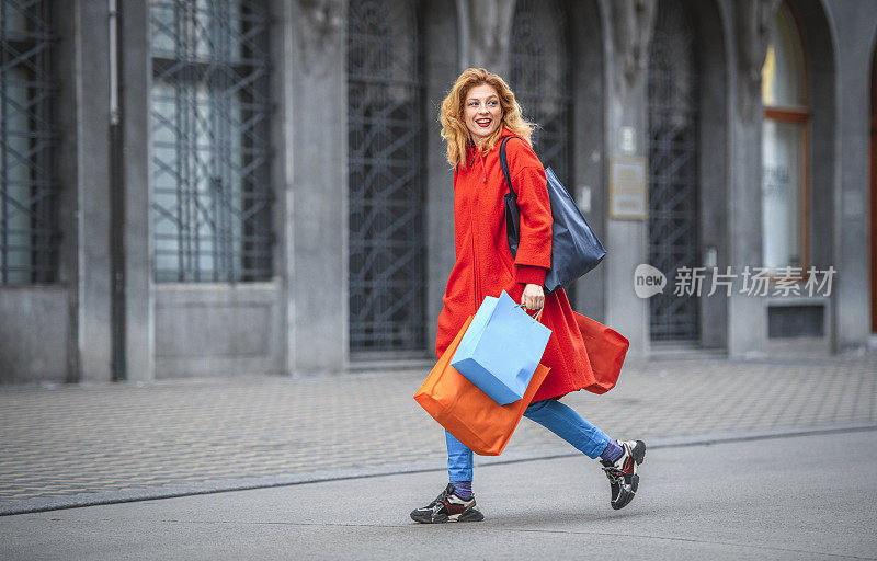 金发白种女人拿着购物袋，走在城市里