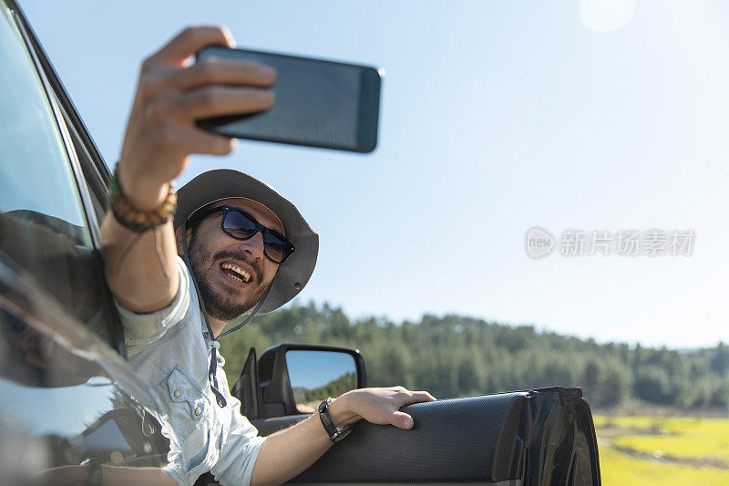 开车旅行时，一名男子一边自拍一边用智能手机发送信息