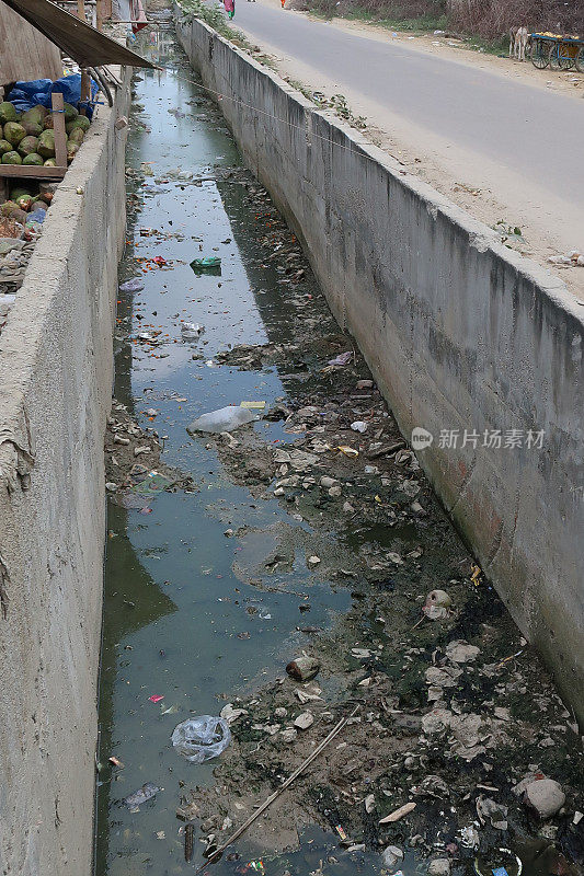 这是在公路和挤满了垃圾和瓦砾的市场摊位之间的水道，被污染的河流，印度德里的荒地