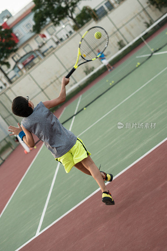 一个男孩正和他的教练在硬地打网球