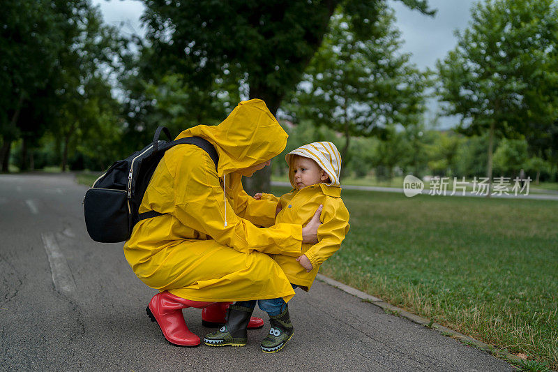 母亲和一个孩子。穿着雨衣的母子在公园里手牵着手