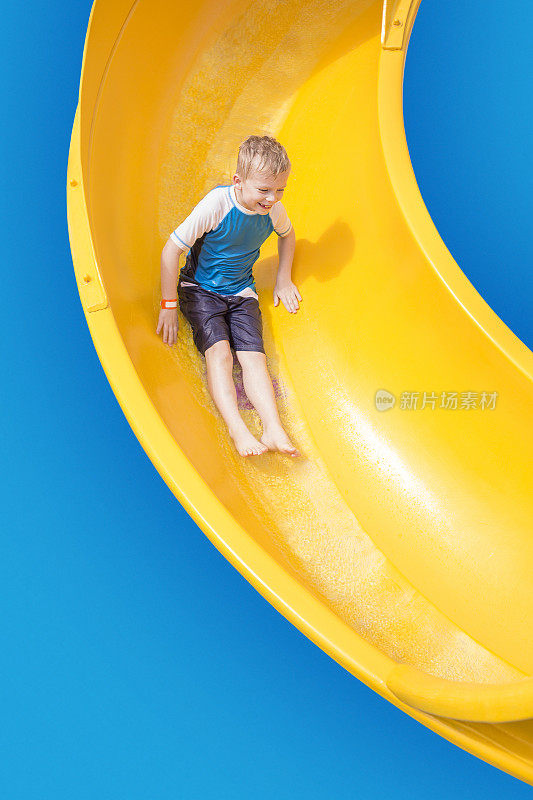 微笑的小男孩骑下黄色的水滑梯