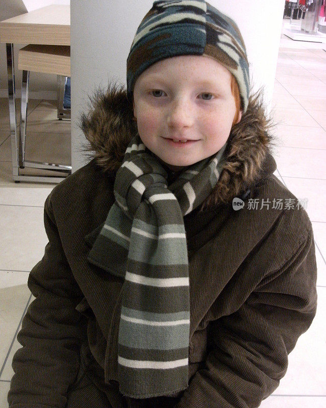 小男孩穿着绿色的冬衣，戴着帽子，围着围巾