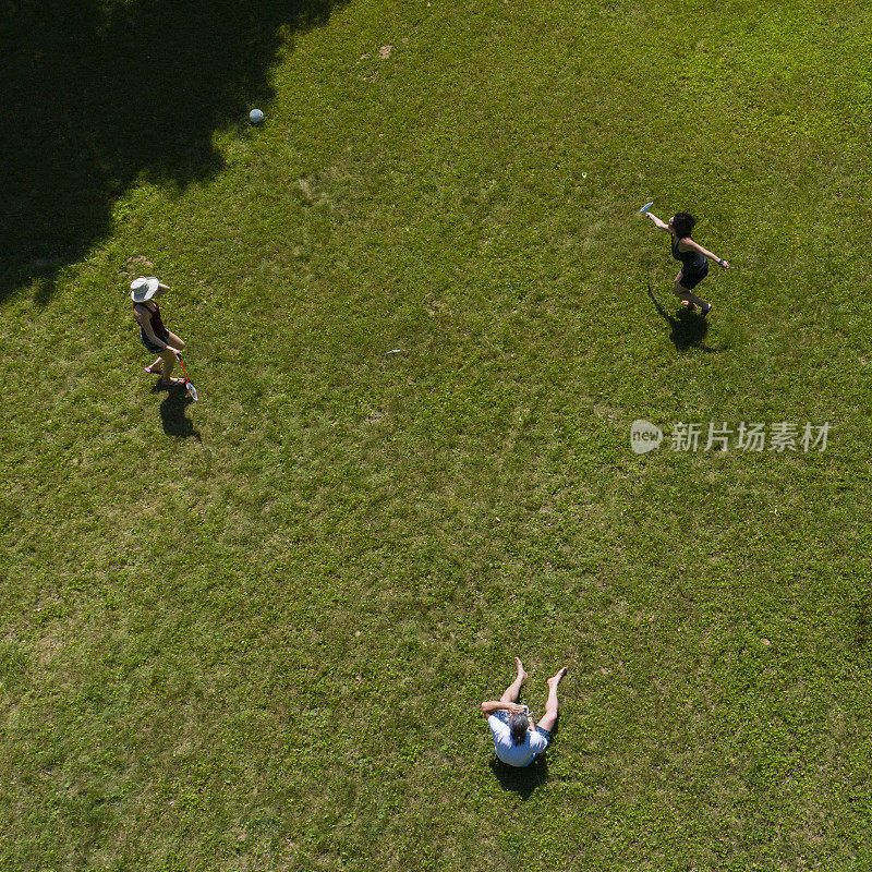 两个女人在草坪上打羽毛球，一个男人在看比赛。俯视图正上方，无人机拍摄