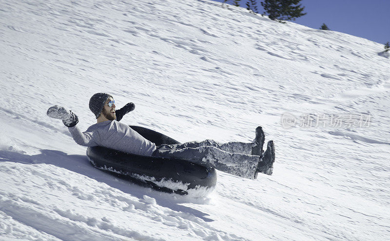 一个年轻人坐着黑色的管子从雪山上滑下来