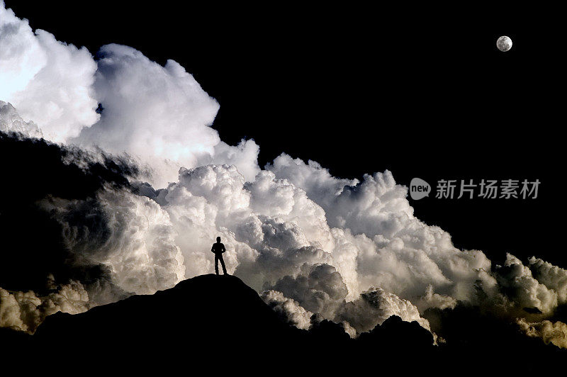 站在山上的人的剪影映衬着汹涌的暴风云