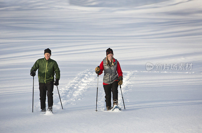男人和女人在一个阳光明媚的冬天穿雪鞋。