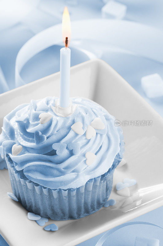 男孩的第一个生日蛋糕有蜡烛，蓝色糖霜和丝带