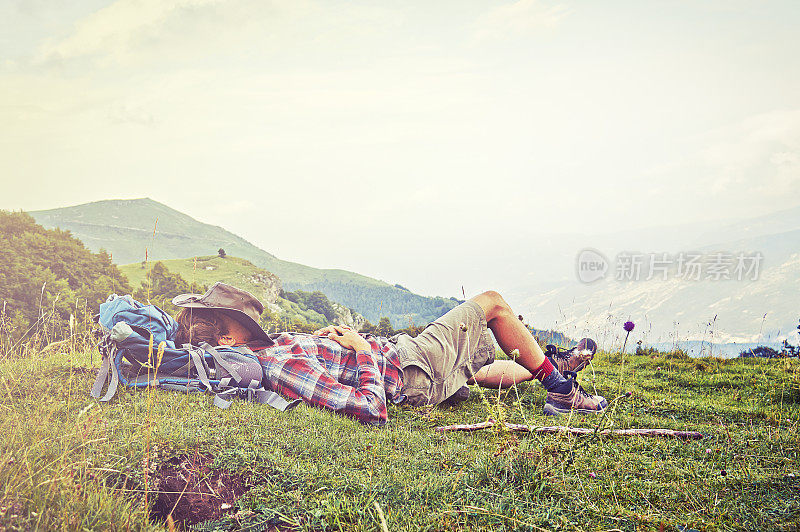 背包徒步者躺在山顶的草地上。