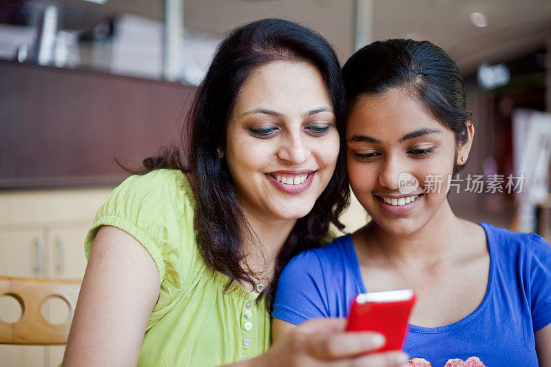 快乐的印度母亲和女儿在食堂发送阅读短信