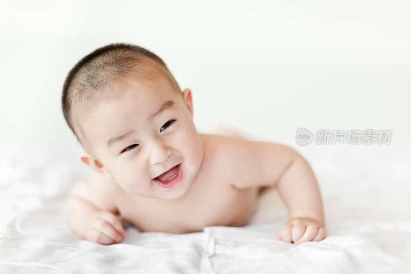 赤裸快乐的小男婴爬在白色的床上