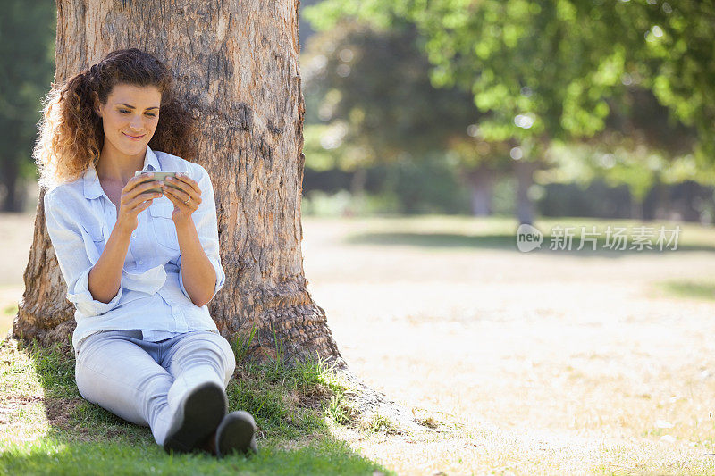漂亮女人坐在树旁，微笑着发短信