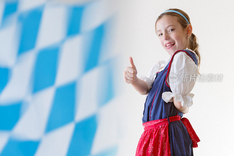 穿着传统服装的巴伐利亚小女孩和巴伐利亚旗帜竖起大拇指