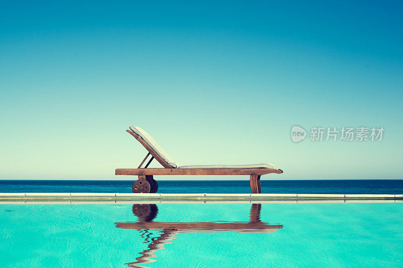 躺椅靠近游泳池，背景是大海和蓝天