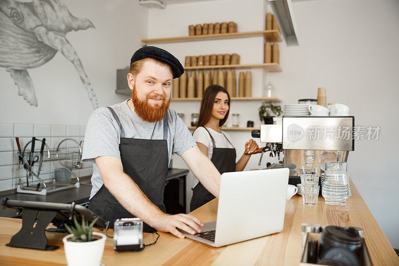 咖啡商业概念-年轻英俊的胡子调酒师，咖啡师或经理工作和计划在笔记本电脑在现代咖啡店。