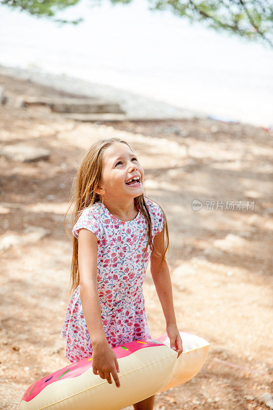 快乐的女孩与甜甜圈形状的充气环与父亲在通往海滩的人行道上玩耍