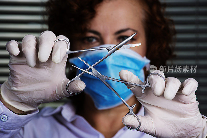女医生戴着蓝色口罩和乳胶手套，用镊子穿手术针