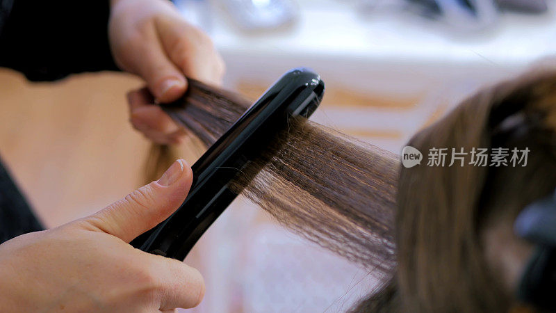 发型师在发廊对顾客的长发使用直发器