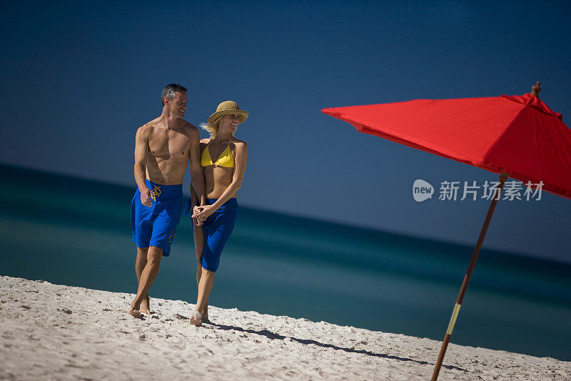 年轻夫妇微笑着，在海滩上牵着手