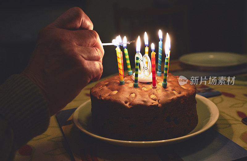 一位退休老人的手在他69岁生日蛋糕上点燃蜡烛。