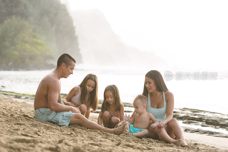 欧亚大陆的父母和他们的孩子在夏威夷海滩的沙滩上玩耍