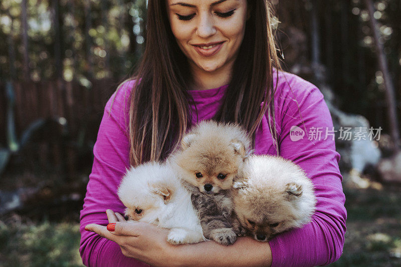 微笑的年轻女子坐着，抱着她的博美犬